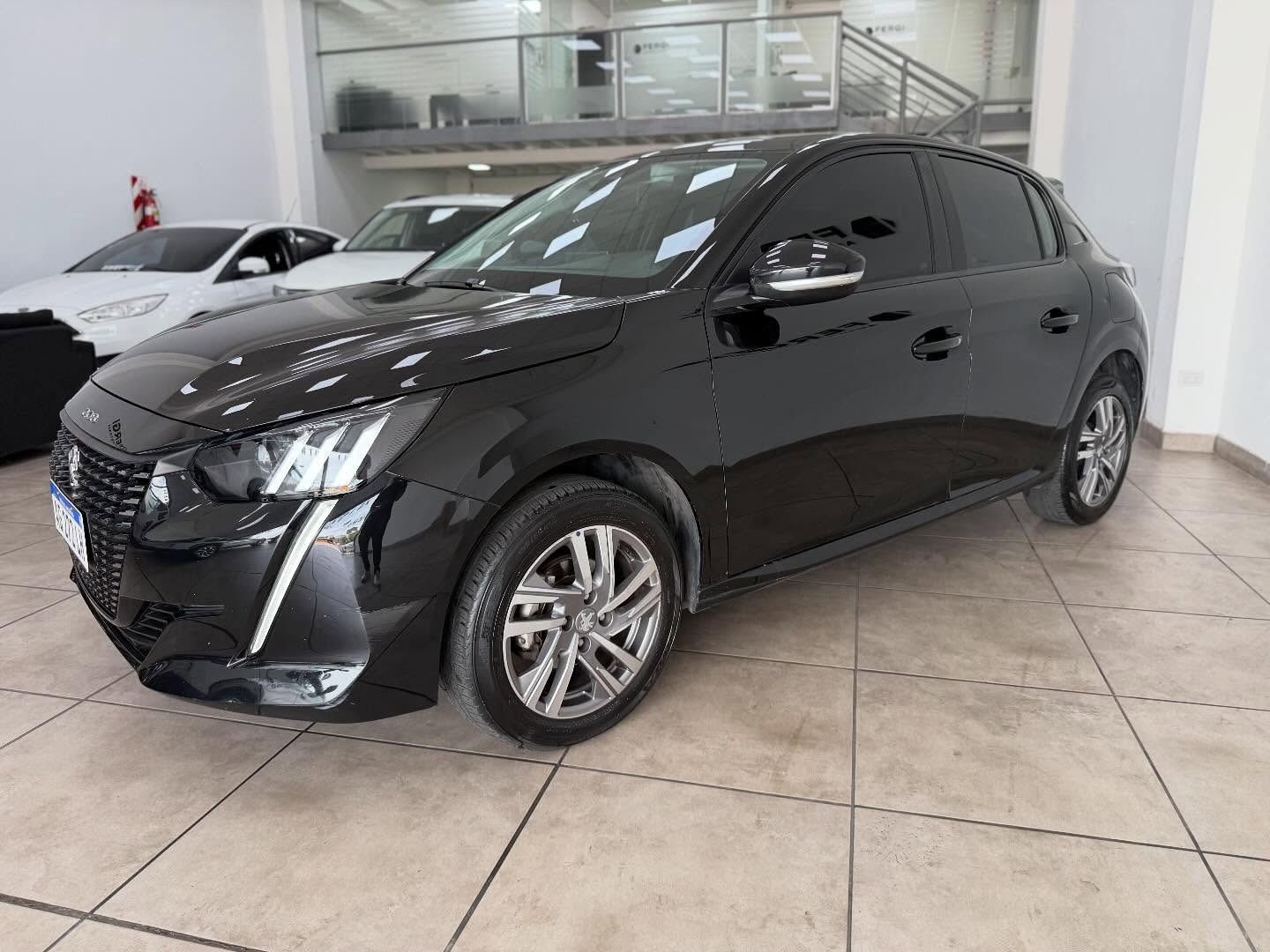 Peugeot 208 negro aparcado en un concesionario, ruedas plateadas y cristales tintados.