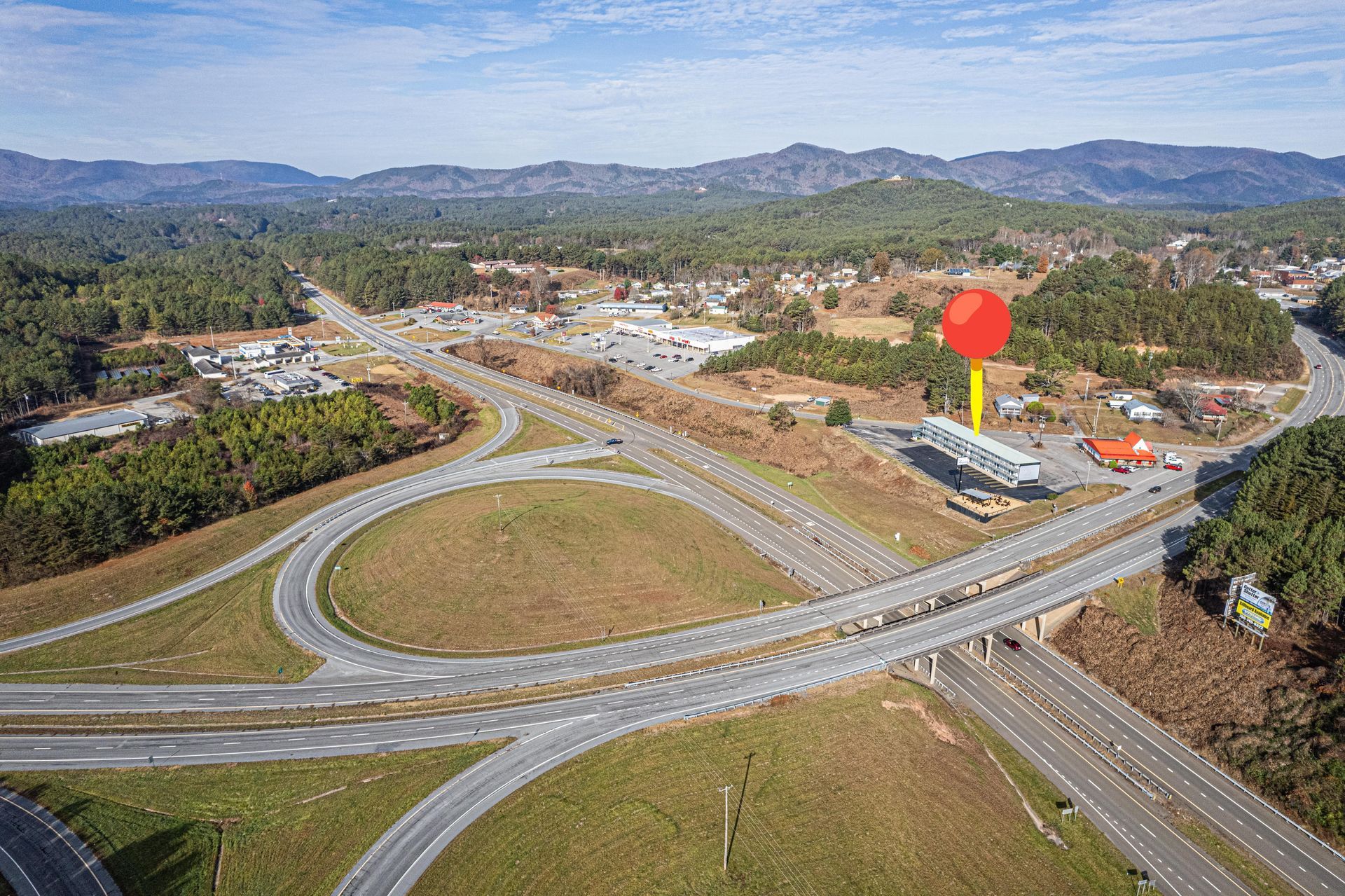 Aerial view of highway interchange with gas station marked by a red pin in a mountainous setting.