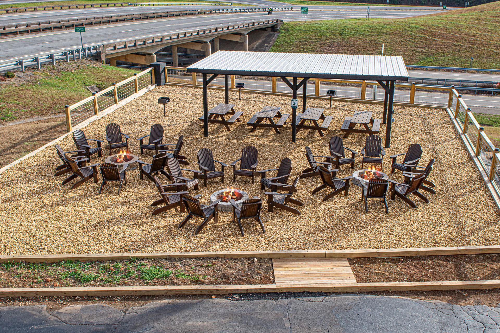 Outdoor seating area with fire pits, chairs, picnic tables under a pergola.