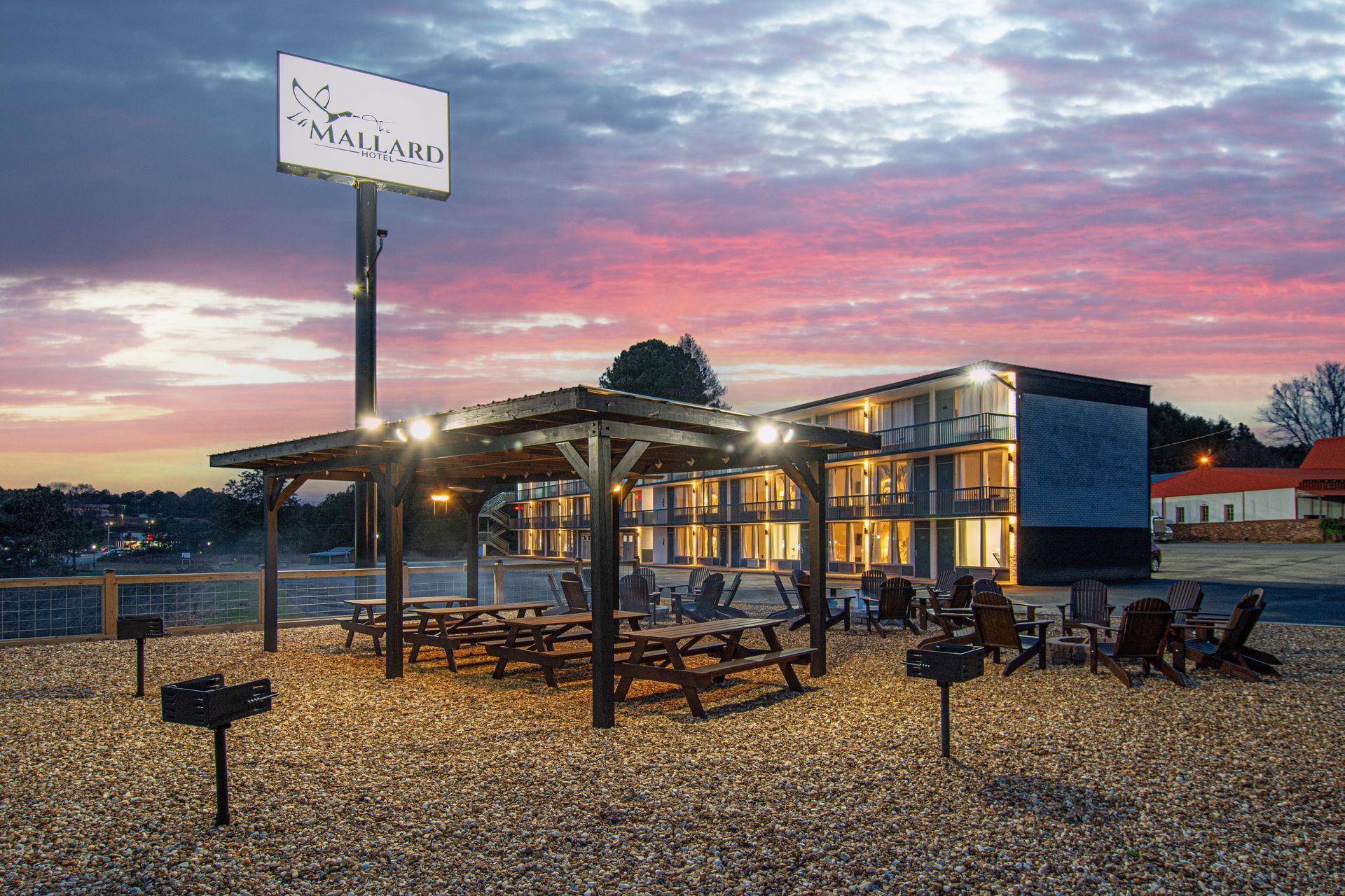 A hotel at dusk with a covered picnic area and sign against a pink and blue sky.
