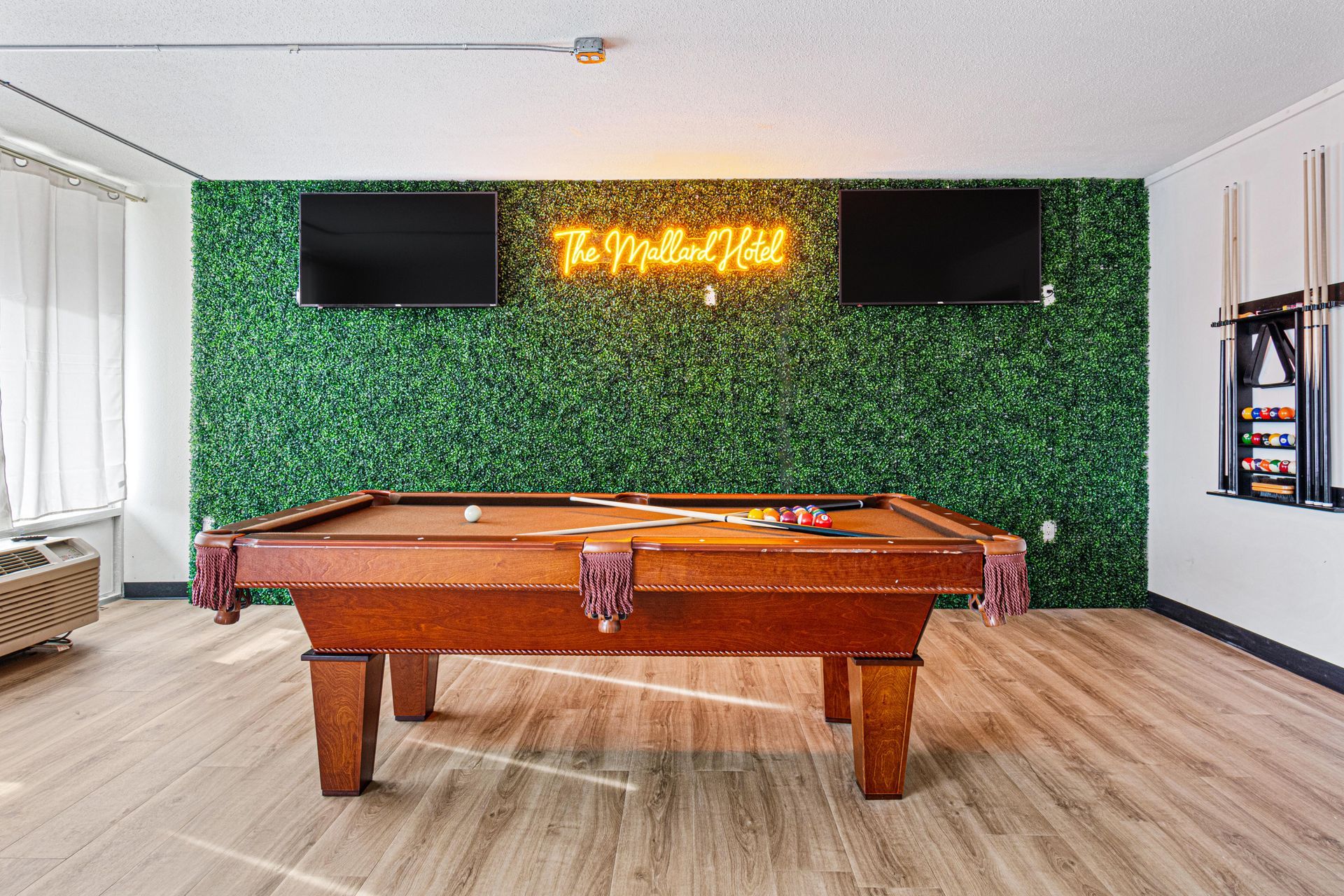 Pool table in a room with green wall, TVs, neon sign, and cue rack.
