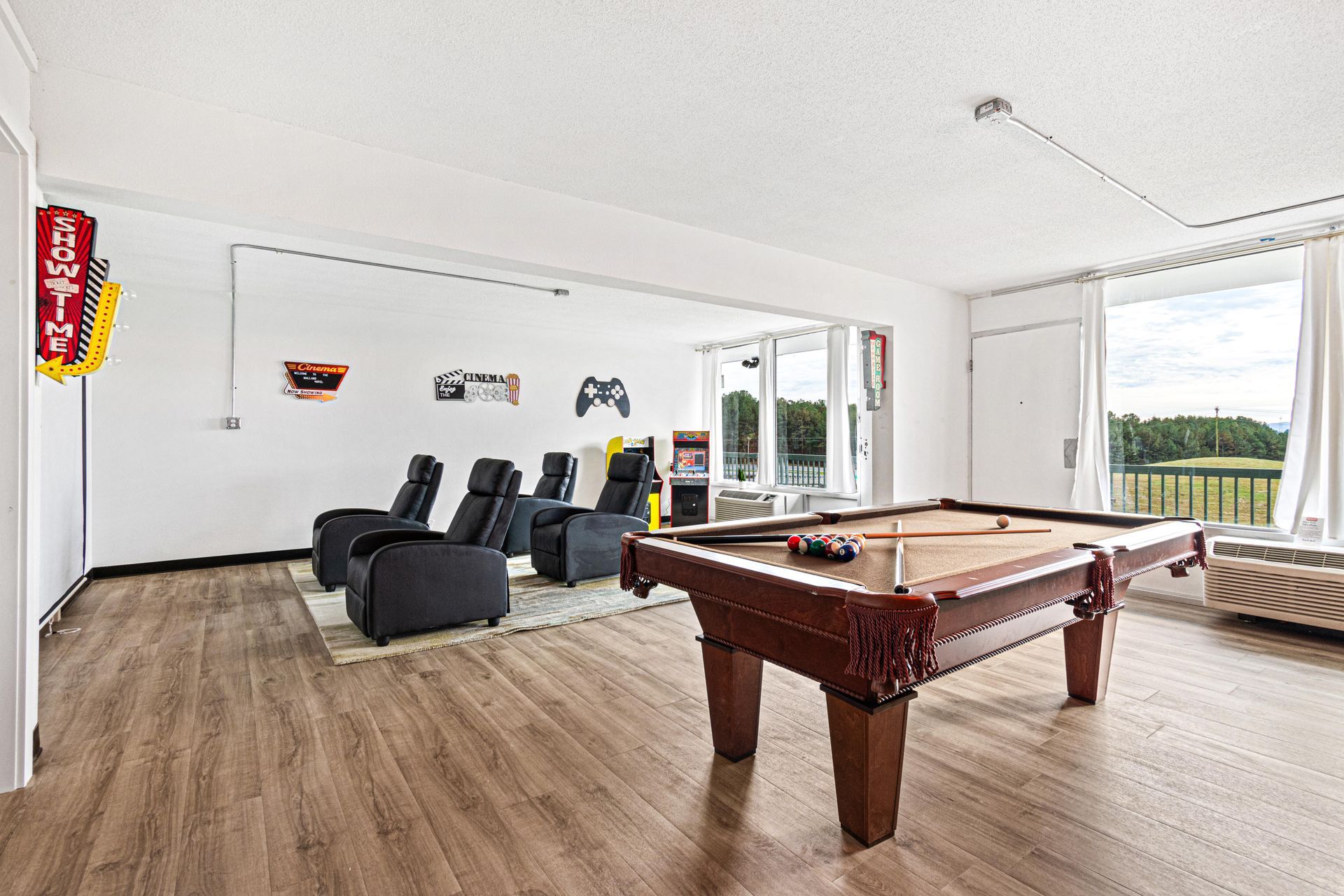 Game room with pool table, reclining chairs, and arcade sign.