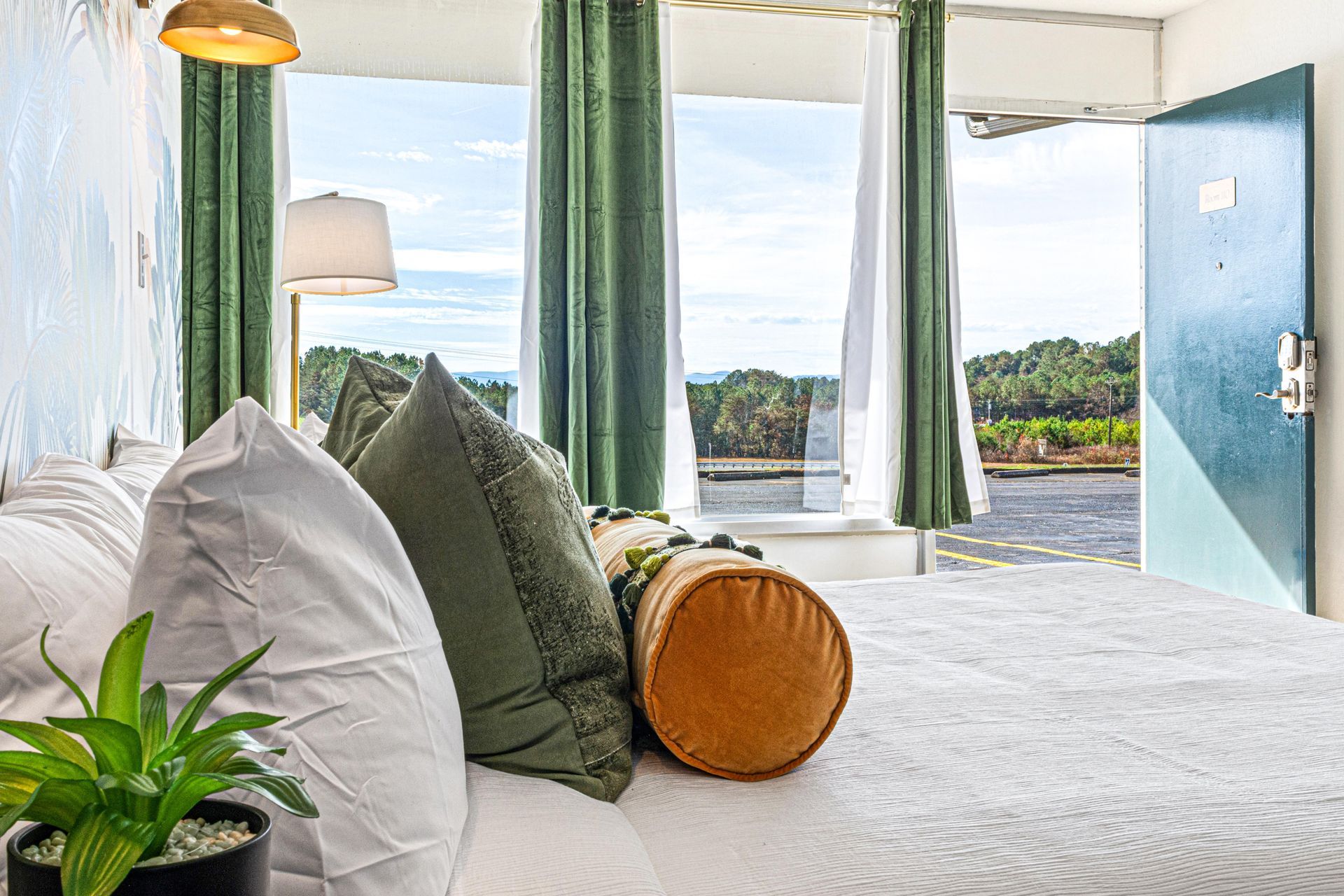 Bedroom with bed, pillows, open door, and view of outdoors. Green curtains, neutral colors.