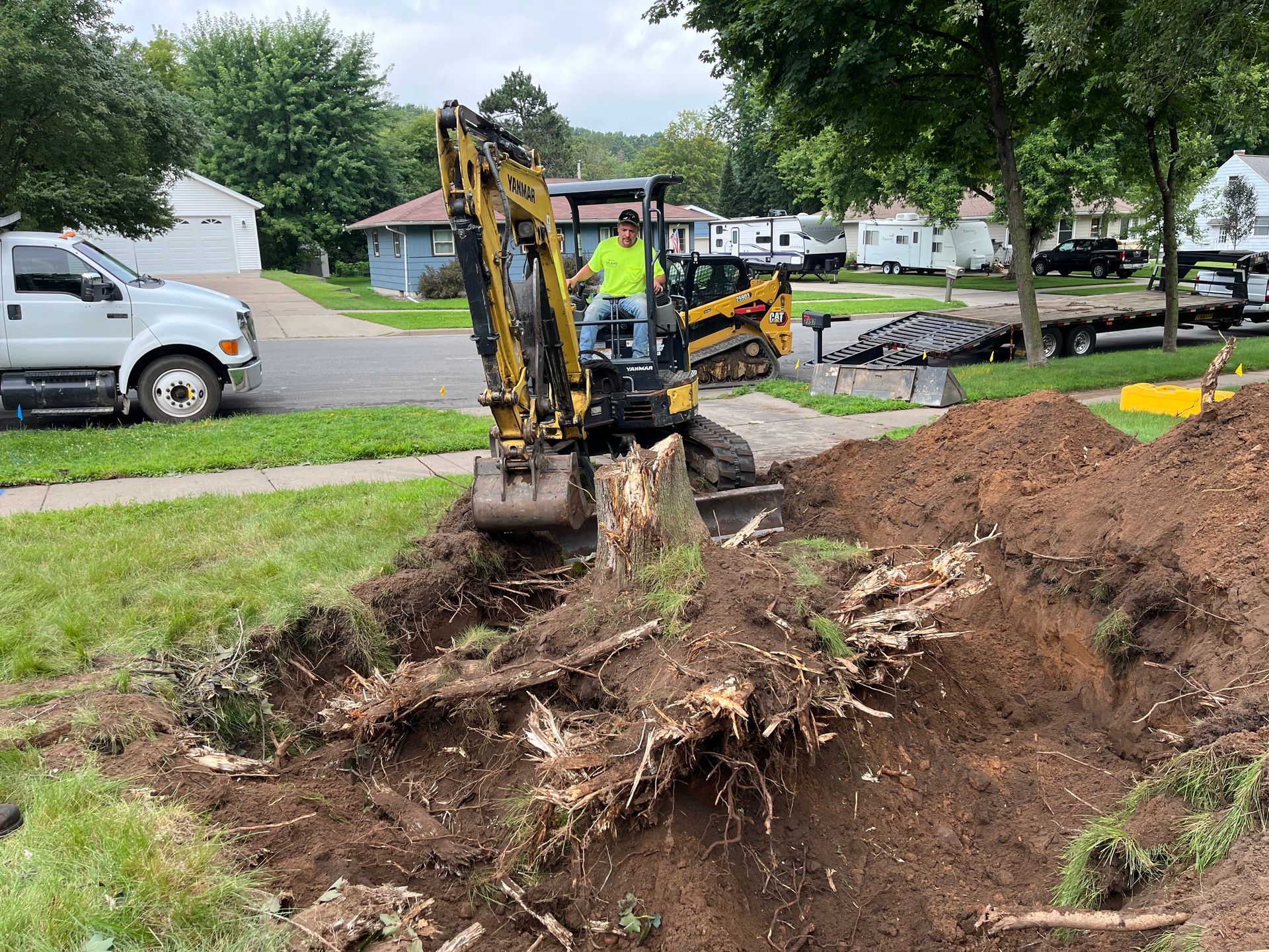 Picture of an excavator working on digging out a tree stump in a residential yard.