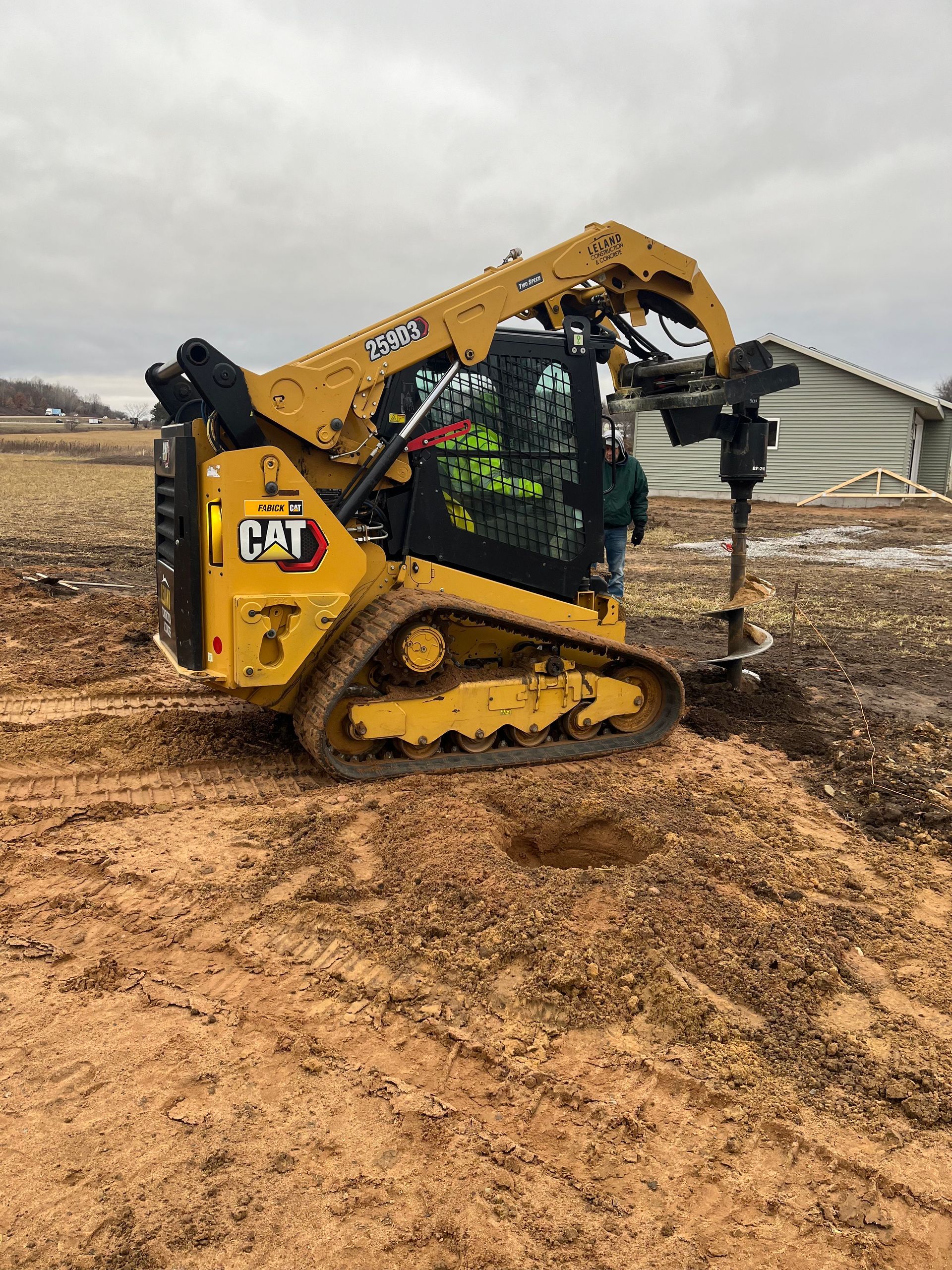 Picture of an auger being operated by someone of the team at Leland construction. They are drilling holes in a field in an industrial zone.