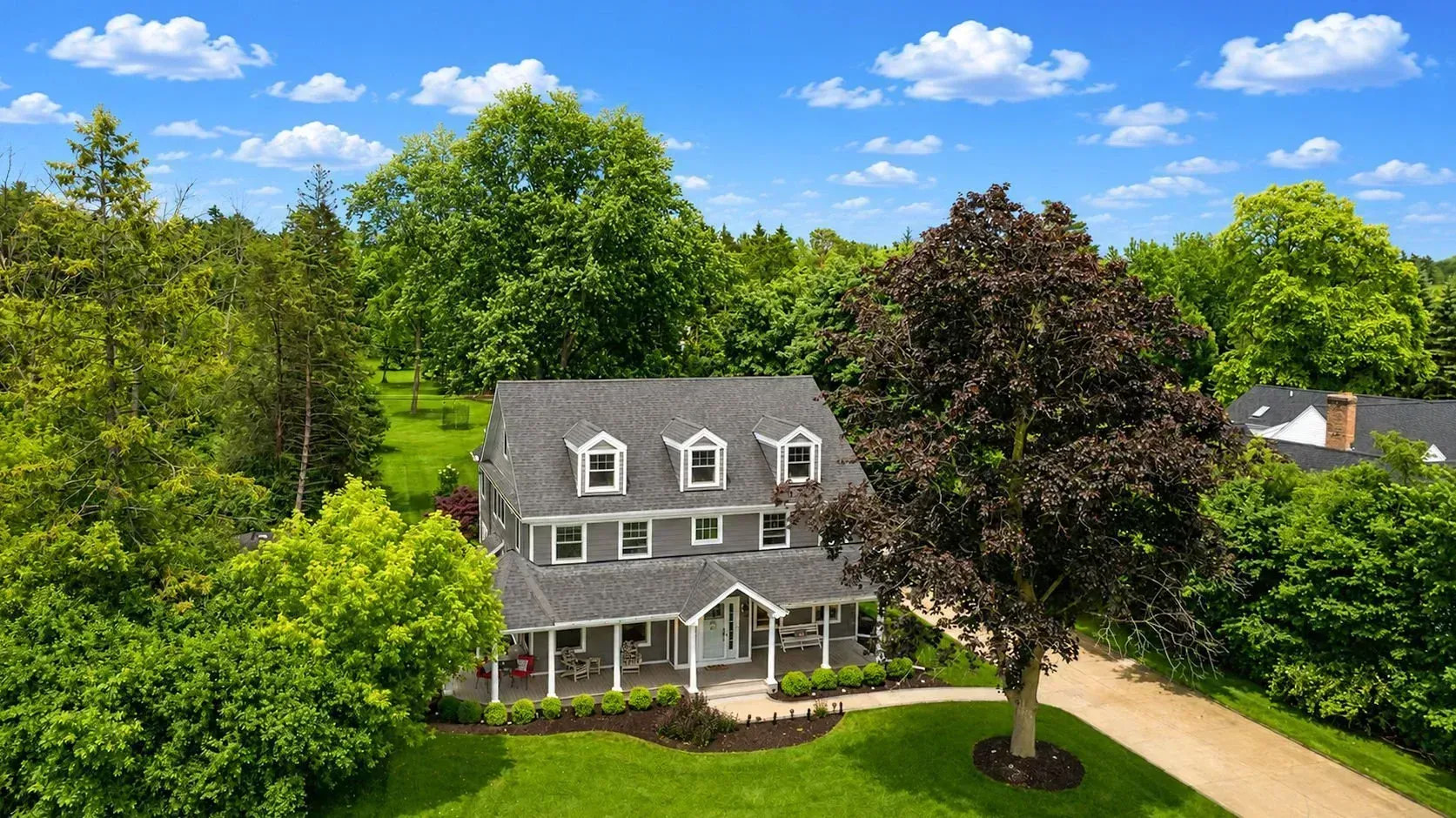 Suburban house with gray siding, detached garage, and a bright green lawn under a blue sky