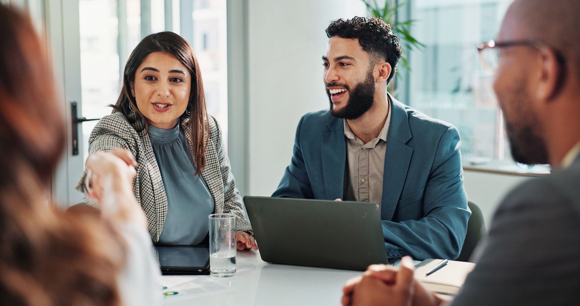 Business colleagues in a meeting, smiling and gesturing, around a table with a laptop. Business colleagues in a meeting, smiling and gesturing, around a table with a laptop.