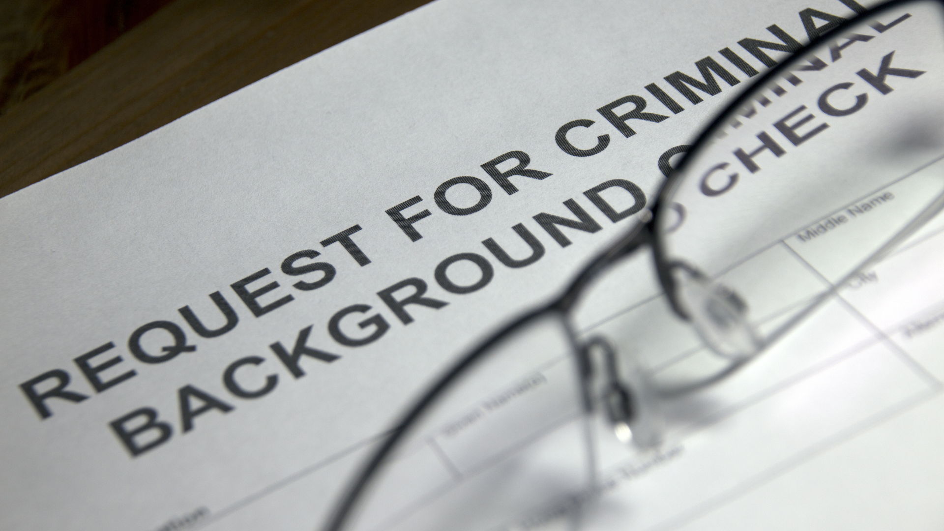 A pair of glasses sits on top of a request for criminal background check form
