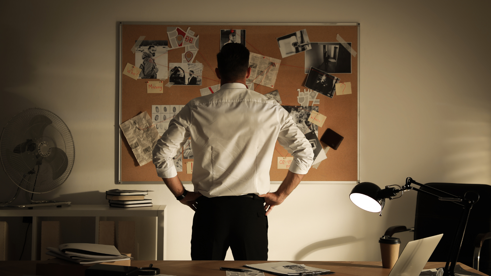 A man is standing in front of a bulletin board in an office.