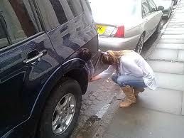 A woman is kneeling down next to a car on the side of the road.