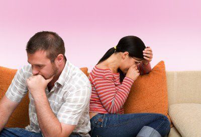 A man and a woman are sitting back to back on a couch.
