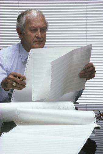 A man is sitting at a desk reading a piece of paper.