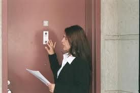 A woman is talking on a doorbell while holding a piece of paper.