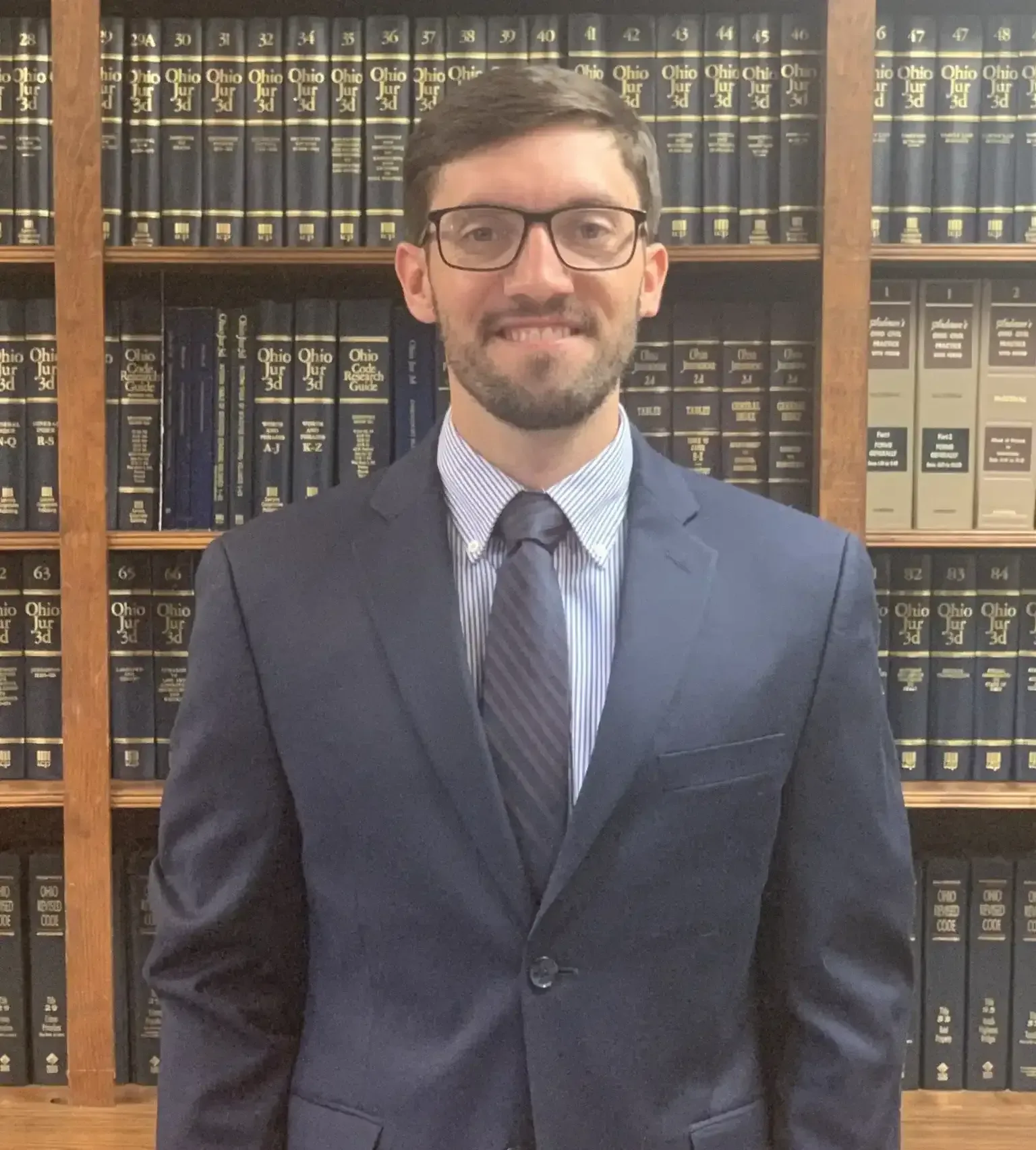 Man in suit and glasses stands in front of a bookshelf filled with books.
