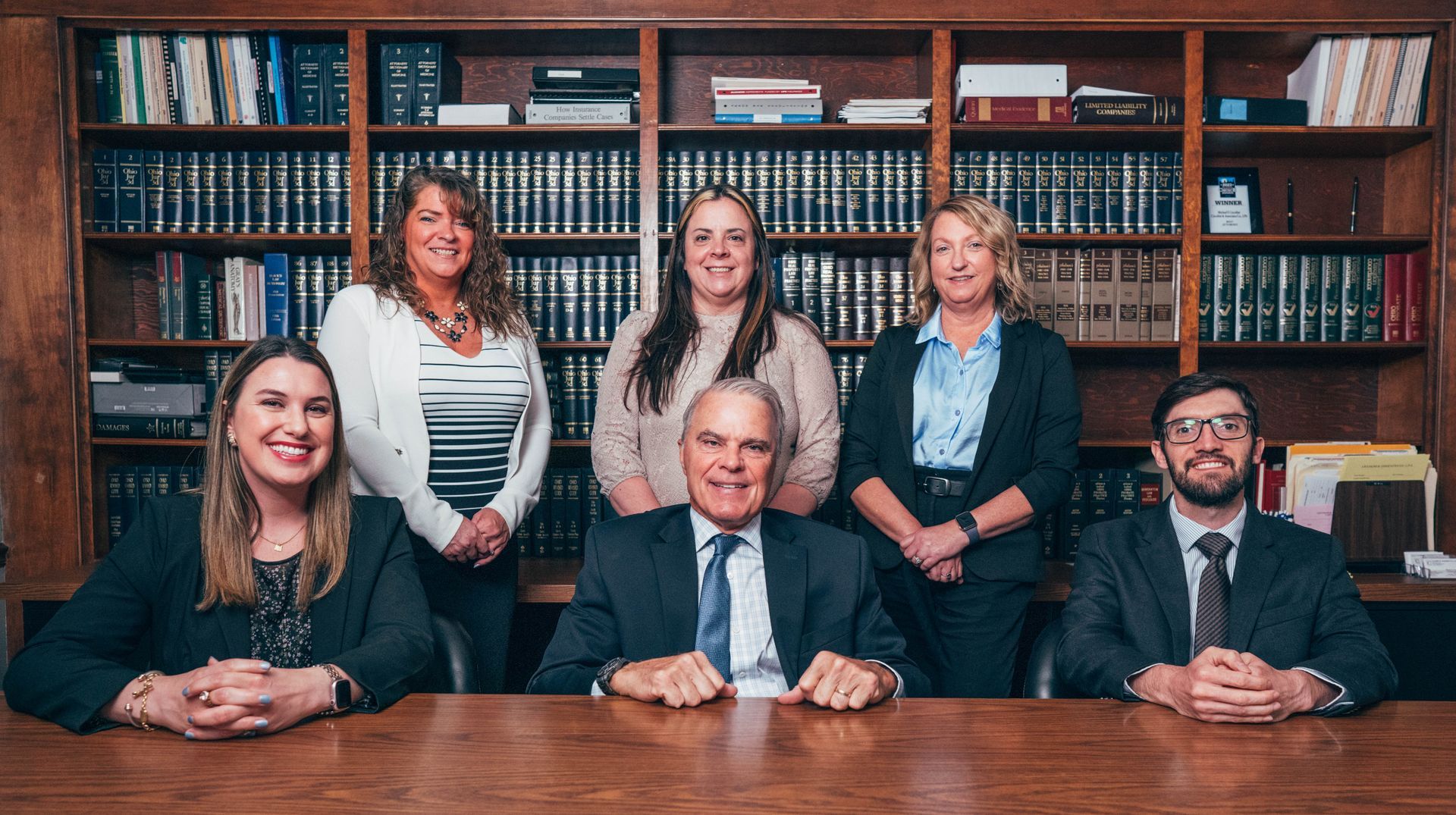 Group of six professionals posing in front of a bookshelf, all wearing business attire.