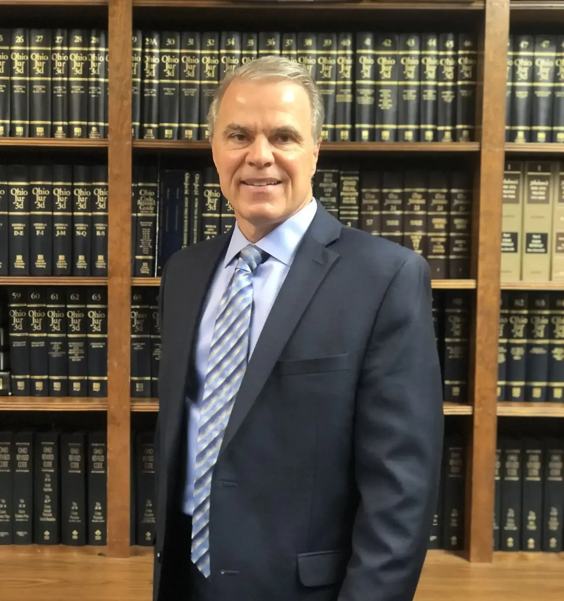 Man in a suit smiles in front of a law library with dark book shelves.