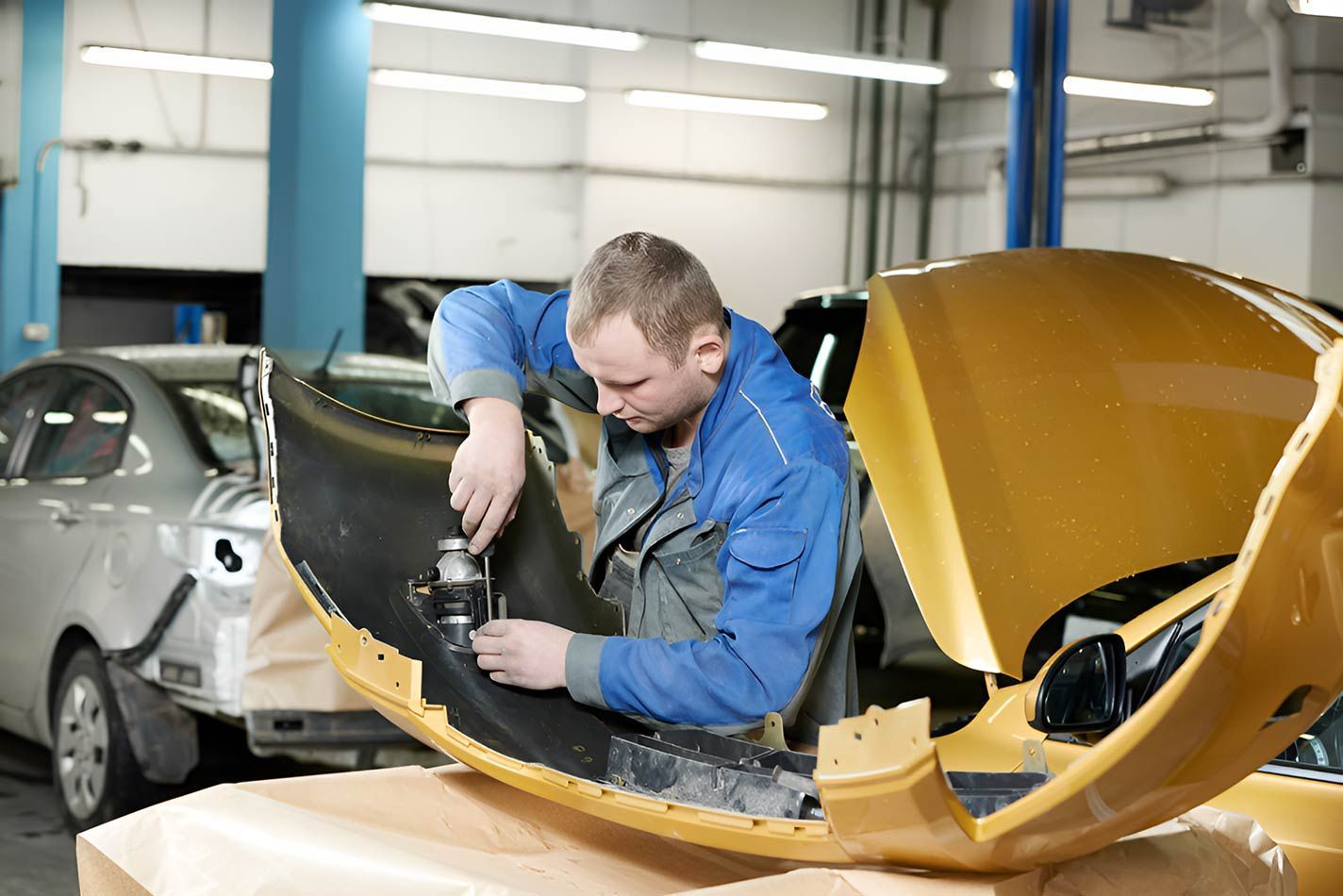A Man Is Working On A Yellow Car In A Garage — Milini's Panel, Paint & Towing in Tully, QLD