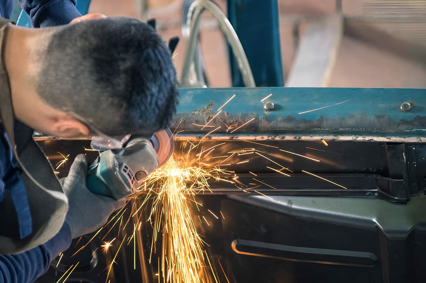 A Man Is Grinding A Piece Of Metal With A Grinder — Milini's Panel, Paint & Towing in Tully, QLD