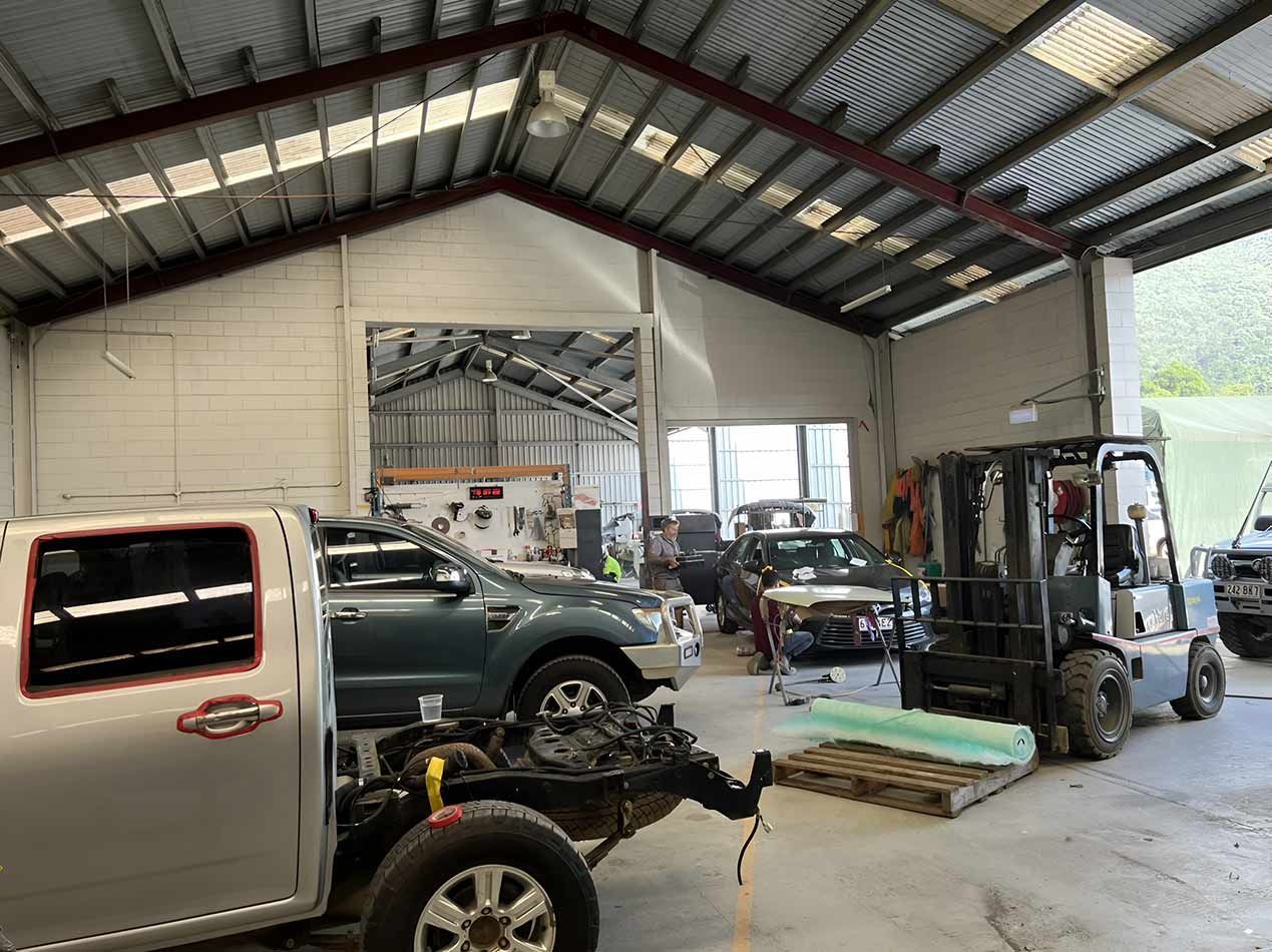 A Truck Is Sitting On A Trailer In A Garage Next To A Forklift — Milini's Panel, Paint & Towing in Tully, QLD