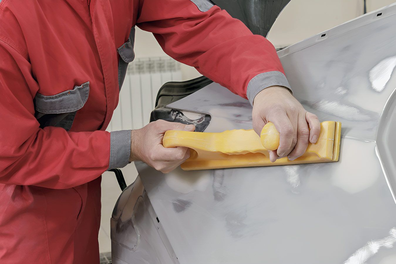 A Man In A Red Suit Is Sanding The Hood Of A Car — Milini's Panel, Paint & Towing in Tully, QLD