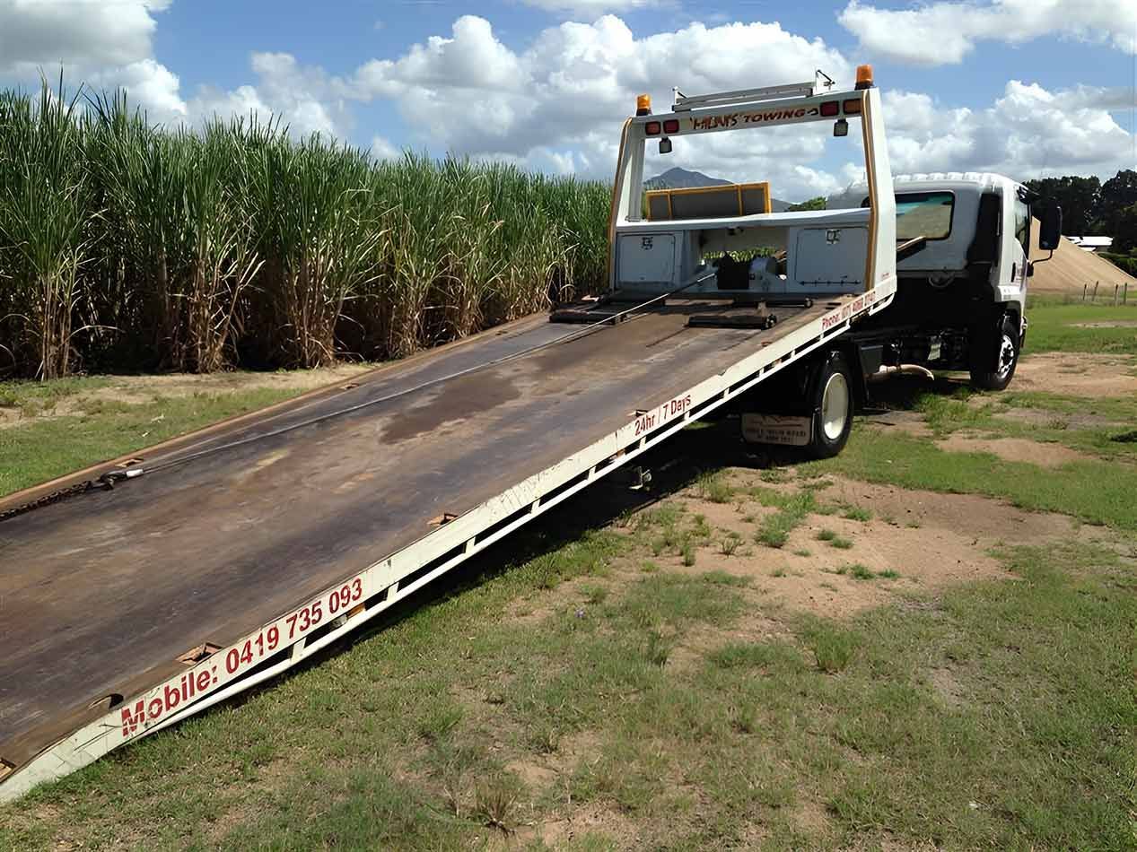 A Tow Truck With A Flat Bed Is Parked In A Grassy Field — Milini's Panel, Paint & Towing in Cairns, QLD