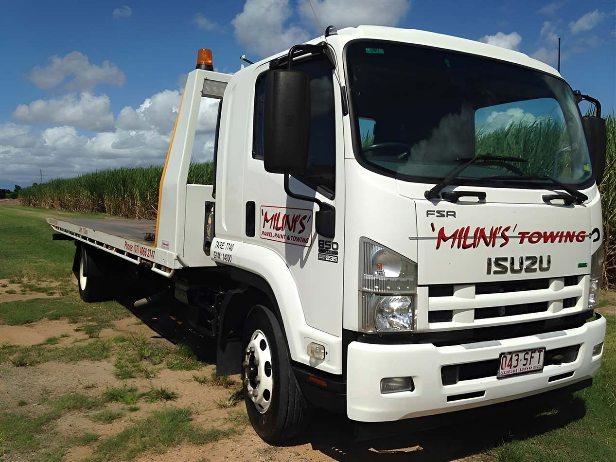 A White Isuzu Tow Truck Is Parked In A Grassy Field — Milini's Panel, Paint & Towing in Ingham, QLD