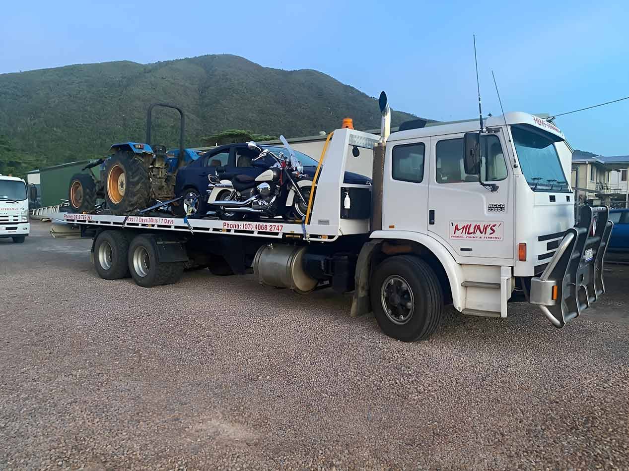 A Tow Truck Is Carrying A Tractor And A Motorcycle On Its Flatbed — Milini's Panel, Paint & Towing in Innisfail, QLD