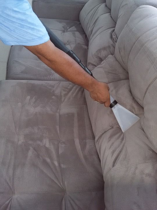 A person is cleaning a couch with a vacuum cleaner