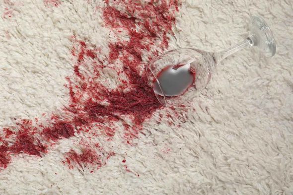 A glass of red wine spilled on a white carpet.