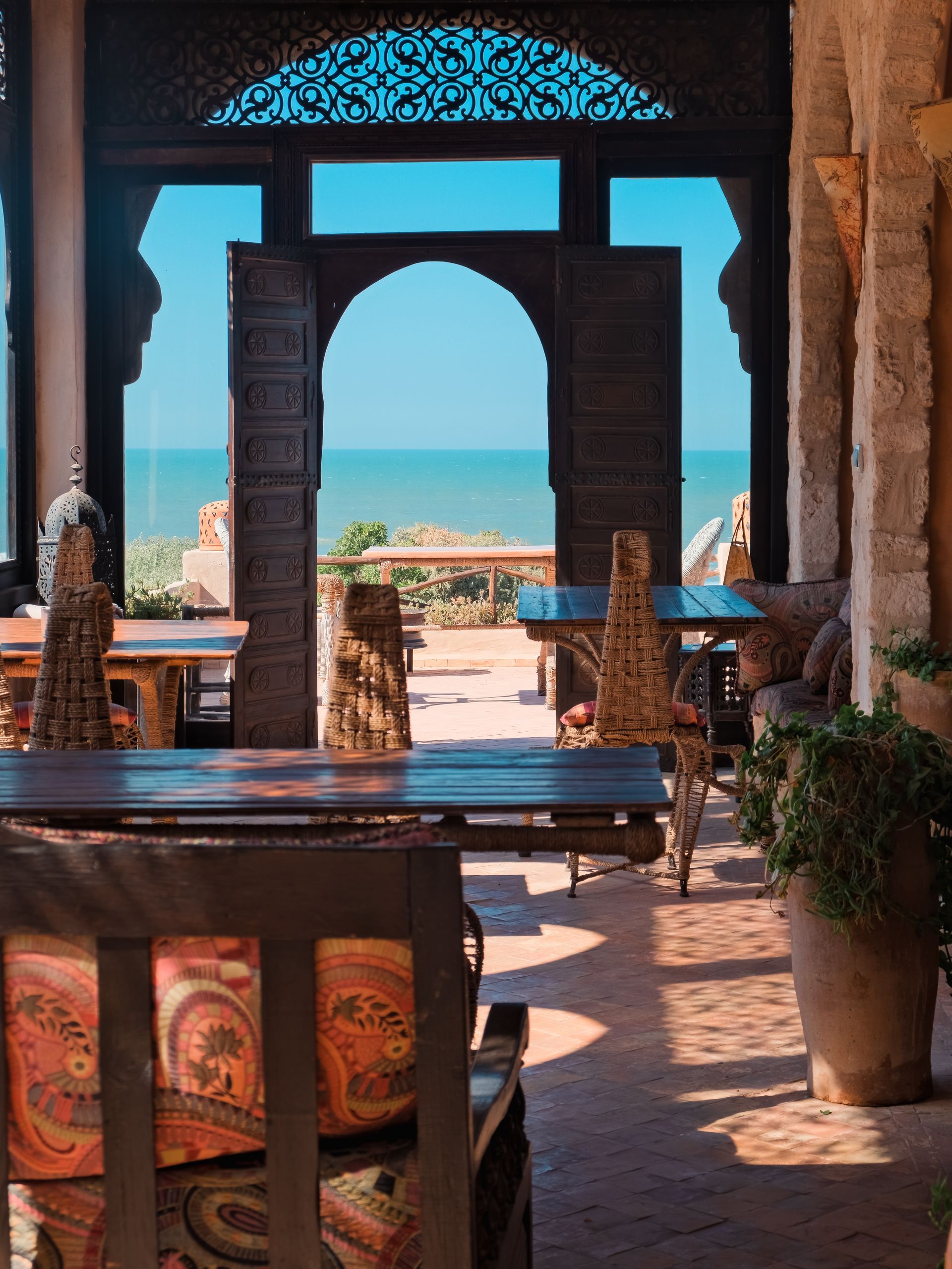 Arched doorway frames ocean view from a sunlit, ornate dining area.