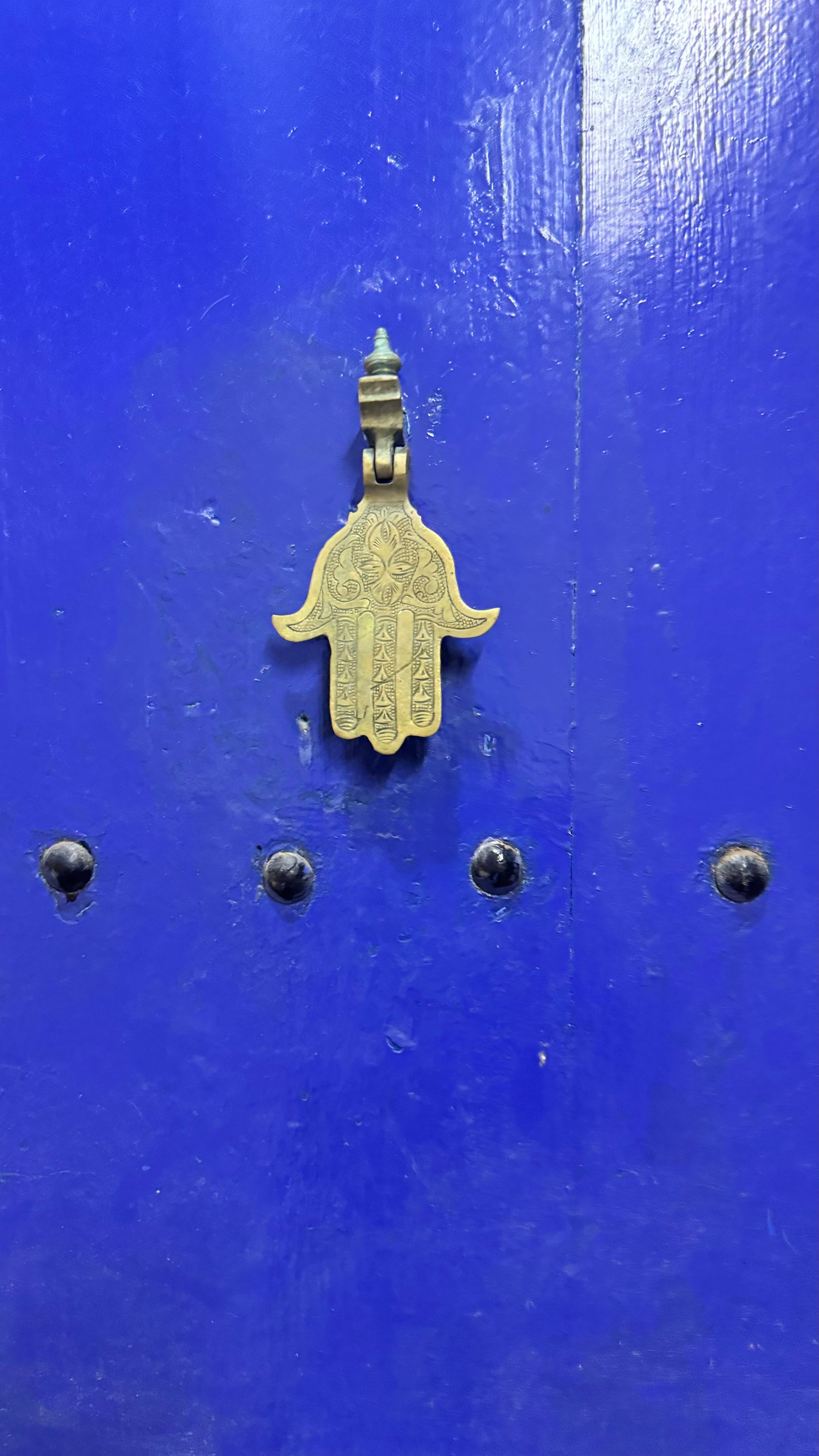 Blue door with a brass Hamsa hand-shaped door knocker and black rivet detail.