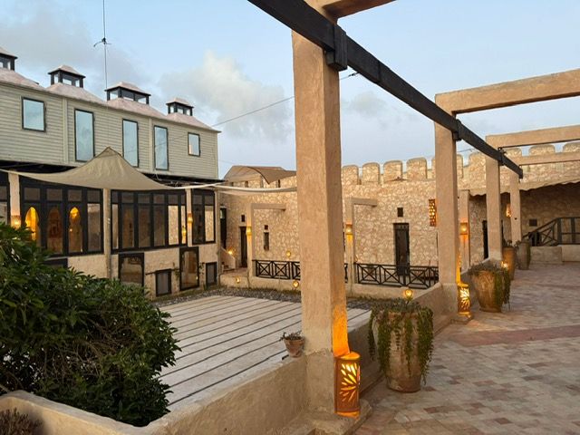 Courtyard with stone walls, wooden accents, and a multi-story building under a cloudy sky.