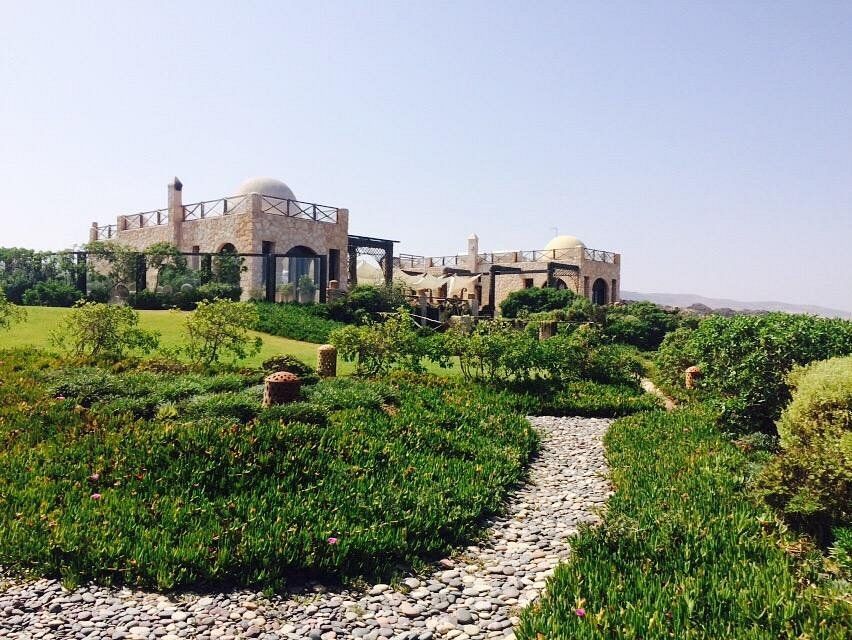 Stone building with domes and towers, surrounded by lush green landscaping and a stone path.