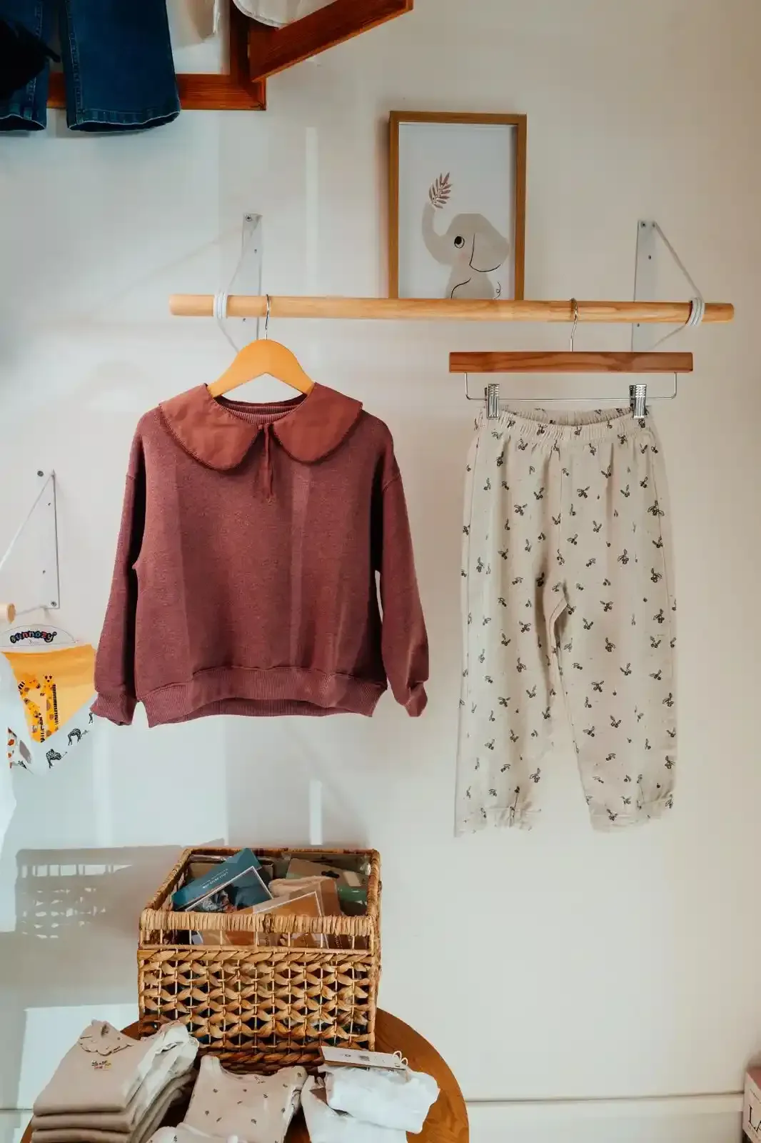 Completo appeso a un attaccapanni di legno: dolcevita a righe, pantaloni verdi e giacca marrone chiaro.