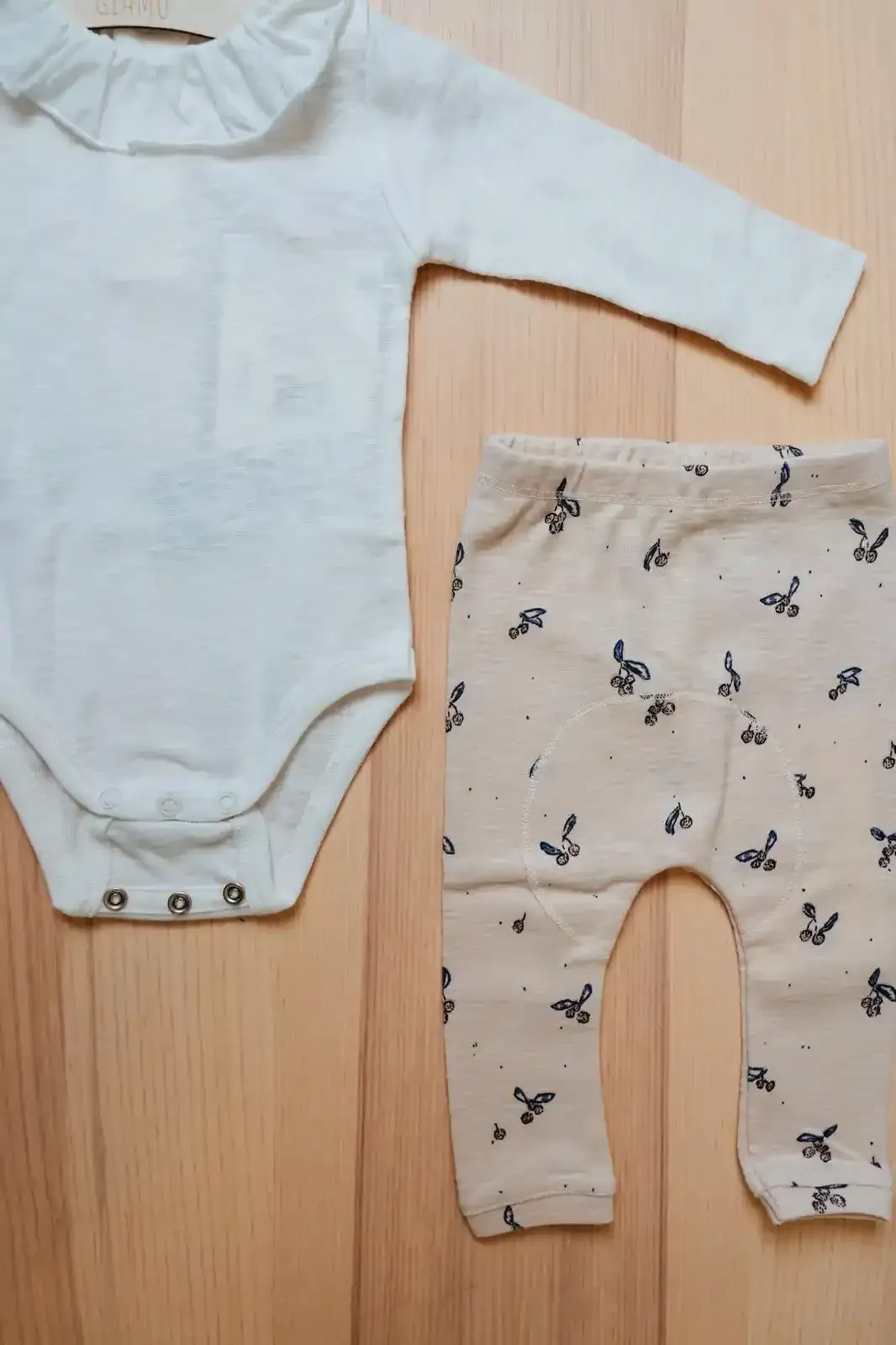 Vestiti appesi su un attaccapanni di legno; sono visibili un vestito rosa con colletto bianco, rifiniture verdi e un maglione grigio.