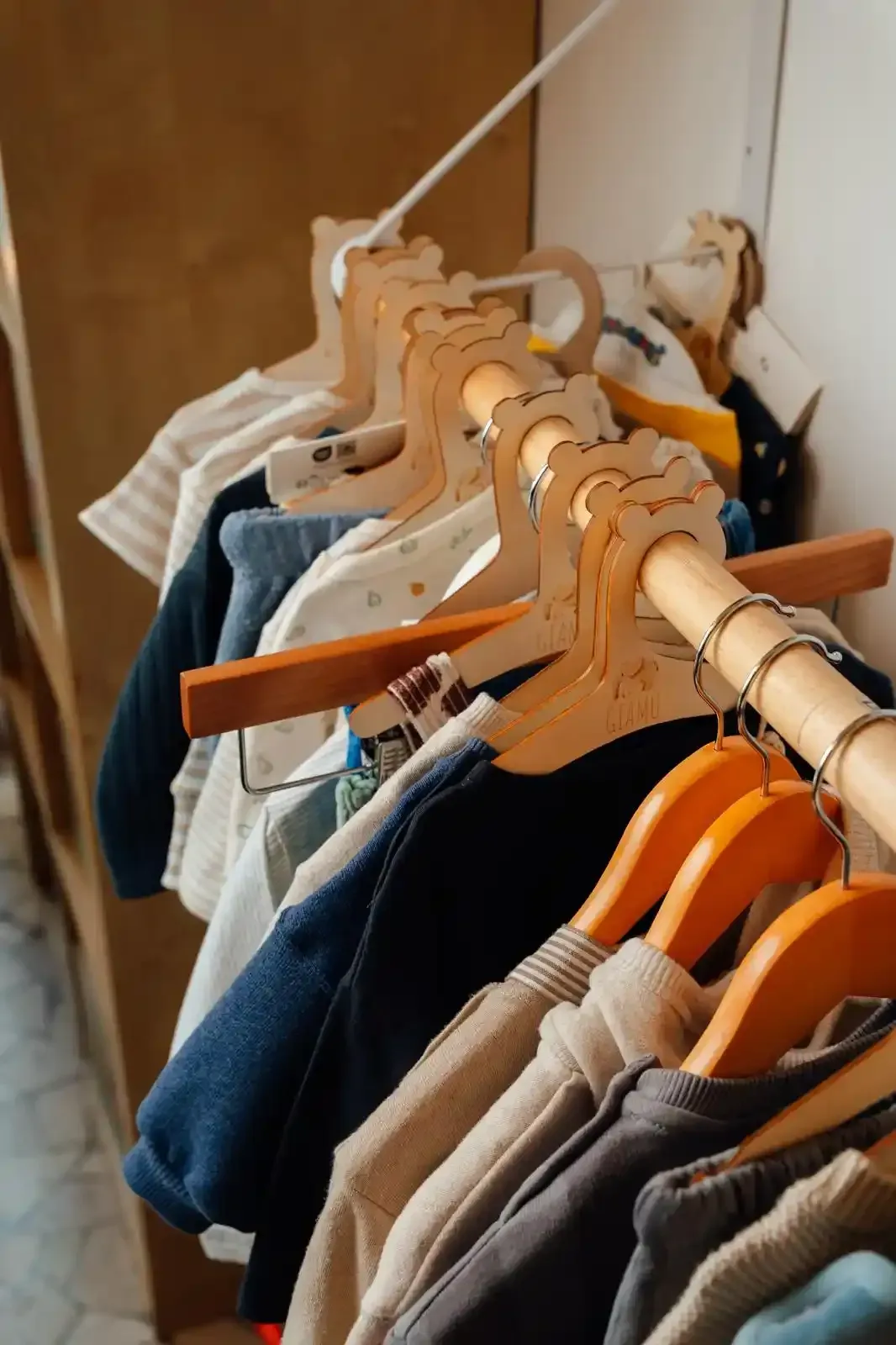 Appendiabiti in legno con vestiti per bambini, tra cui un maglione beige e una giacca di jeans blu.
