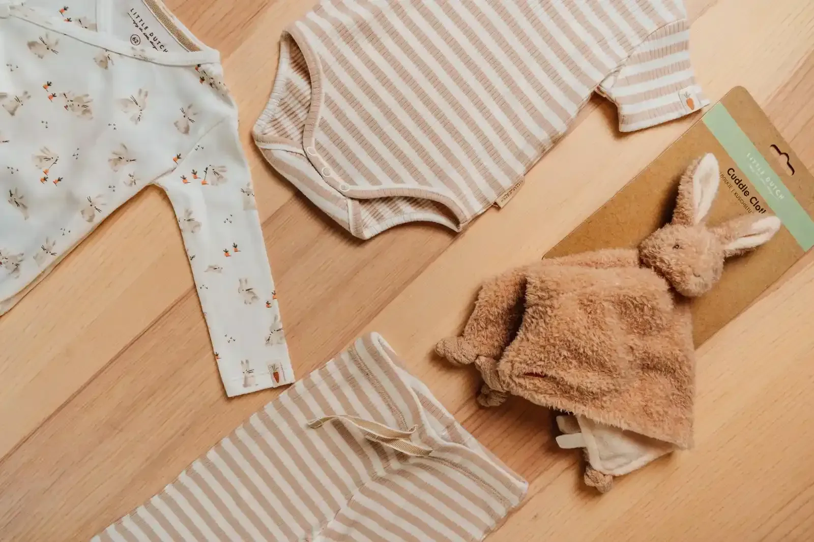 Una salopette di jeans con un maglione bianco fantasia, appeso a una gruccia di legno, accanto a un cappello di pelliccia beige.