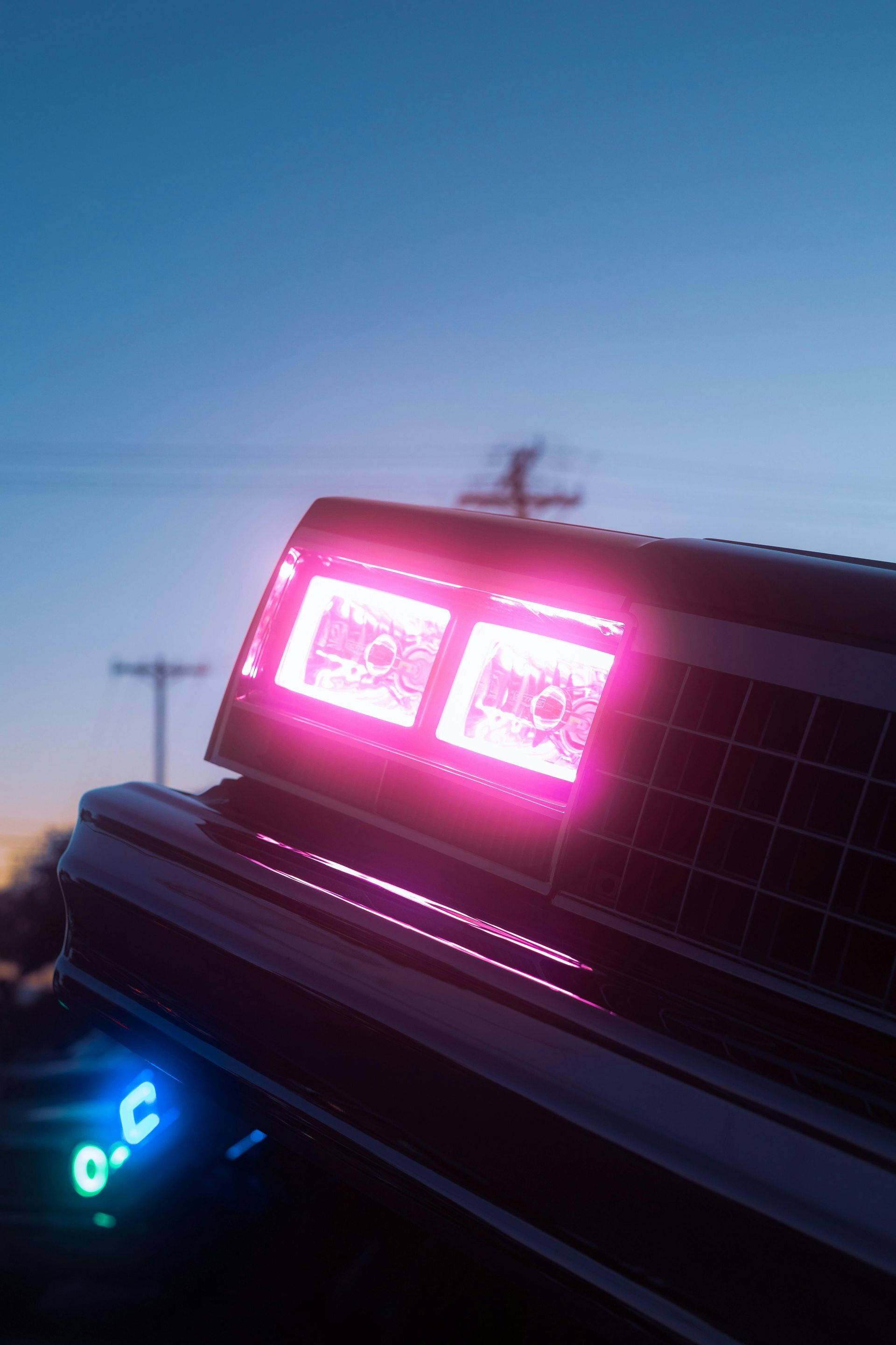 Close-up of a car's glowing pink taillights and blue underglow at dusk.