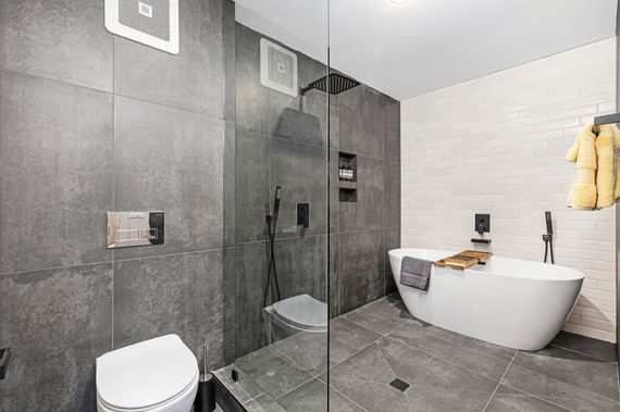 Modern bathroom with gray and white tile, glass shower, white tub, and toilet.