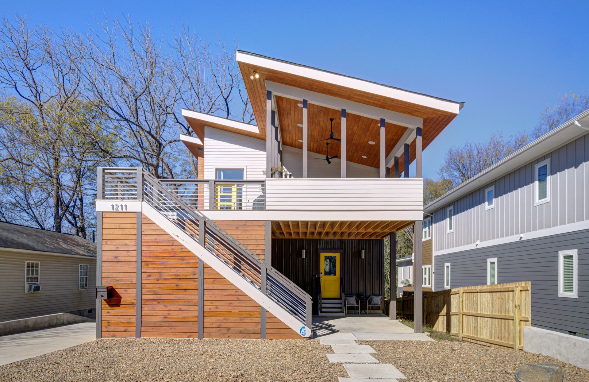 Modern two-story house with a covered porch, wood siding, and a bright yellow front door.