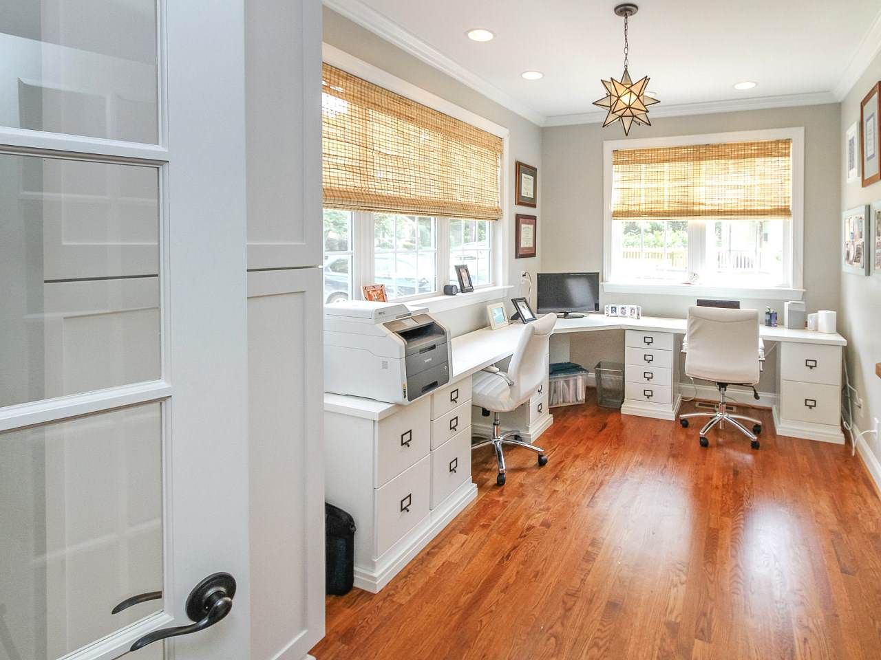 Home office with two desks, bamboo shades, and hardwood floors.