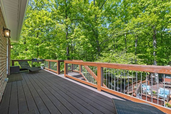 Wooden deck overlooking a lush green forest; lounge chair and grill visible.