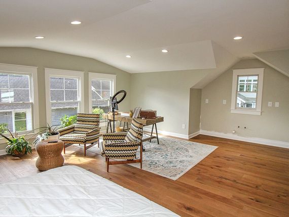 Bright room with hardwood floors, sage walls, and white trim. Two patterned chairs face a desk.