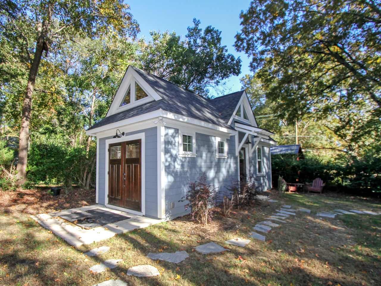 Small blue cottage with a dark wooden door in a wooded setting.