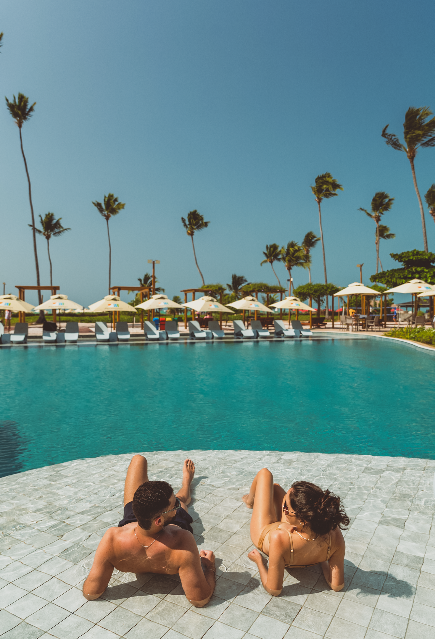 Vista aérea da área da piscina do resort com piscinas, espreguiçadeiras, guarda-sóis e um toboágua.