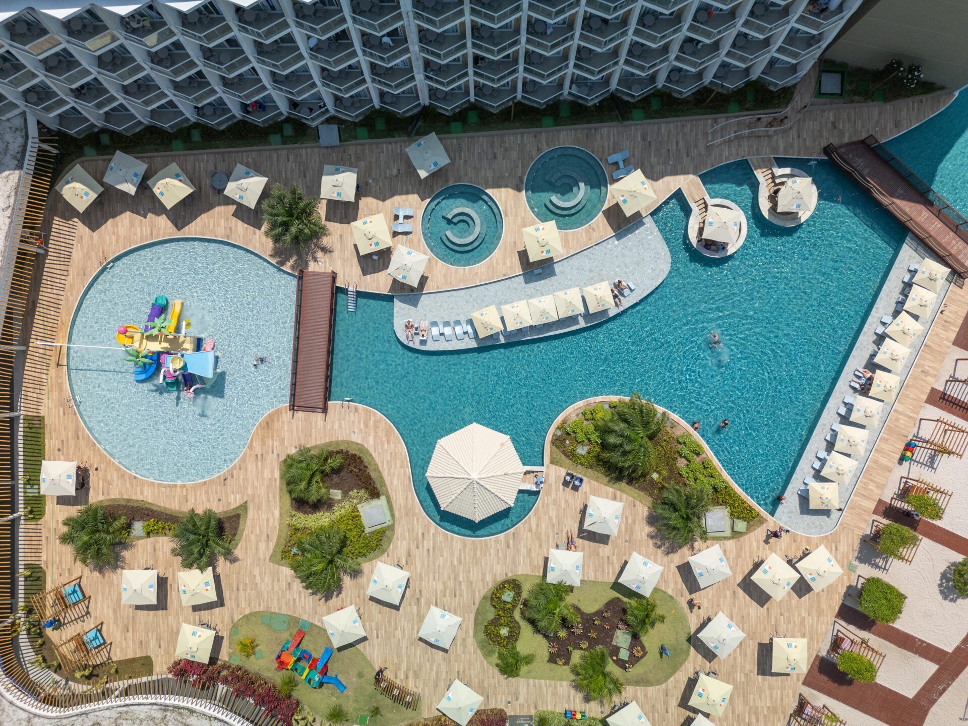 Vista aérea da área da piscina do resort com piscinas, espreguiçadeiras, guarda-sóis e um toboágua.