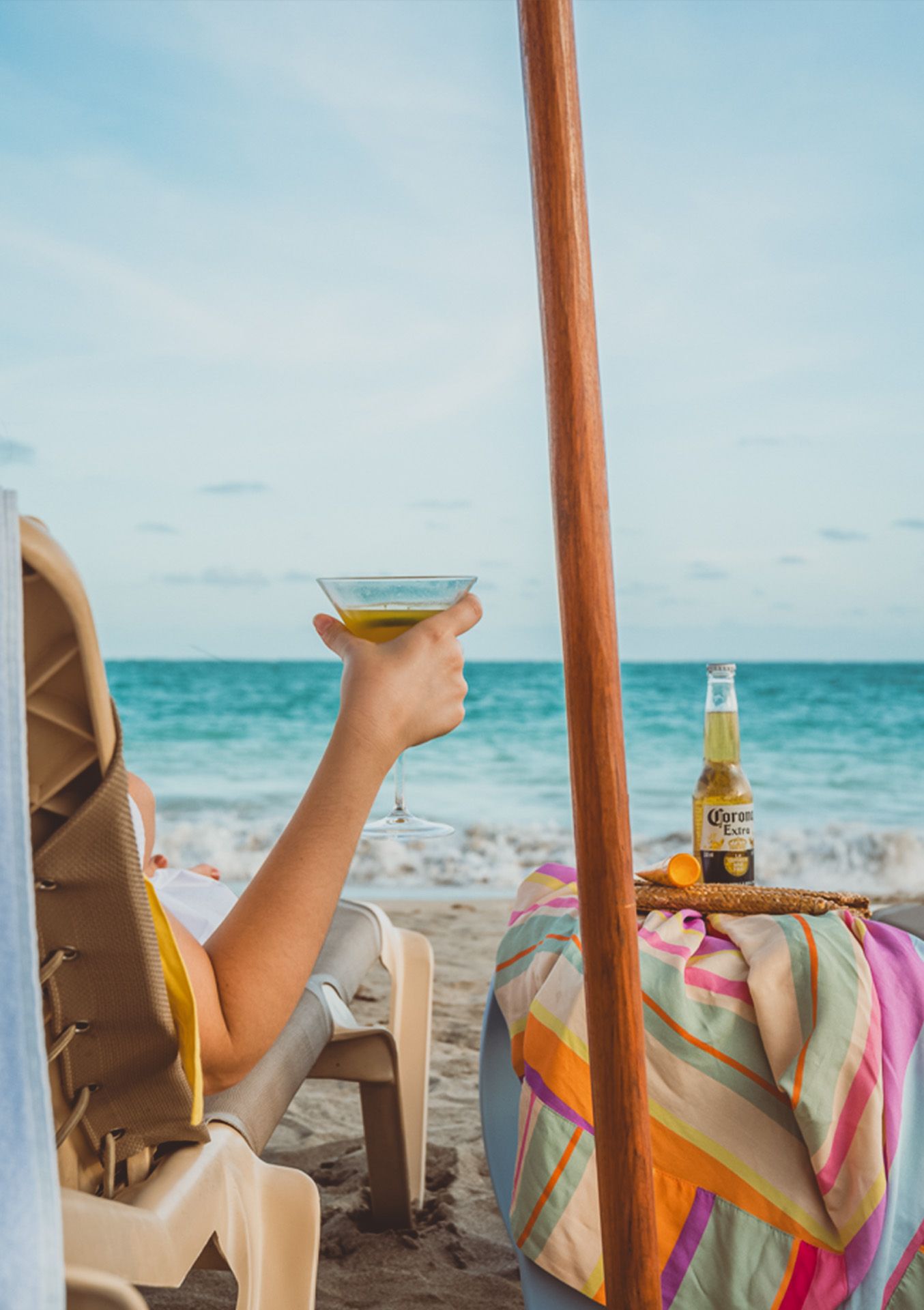 Área de piscina e pátio com espreguiçadeiras, mesas e guarda-sol azul em um hotel.