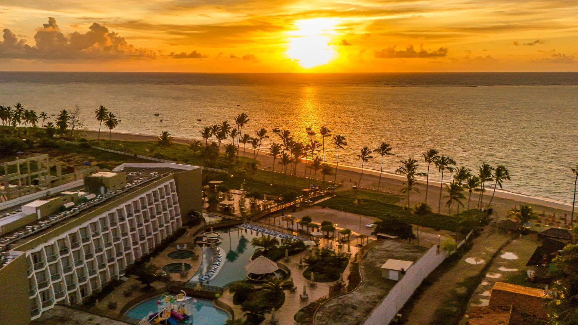 Resort de praia com águas azul-turquesa e praia de areia, pessoas aproveitando o sol.