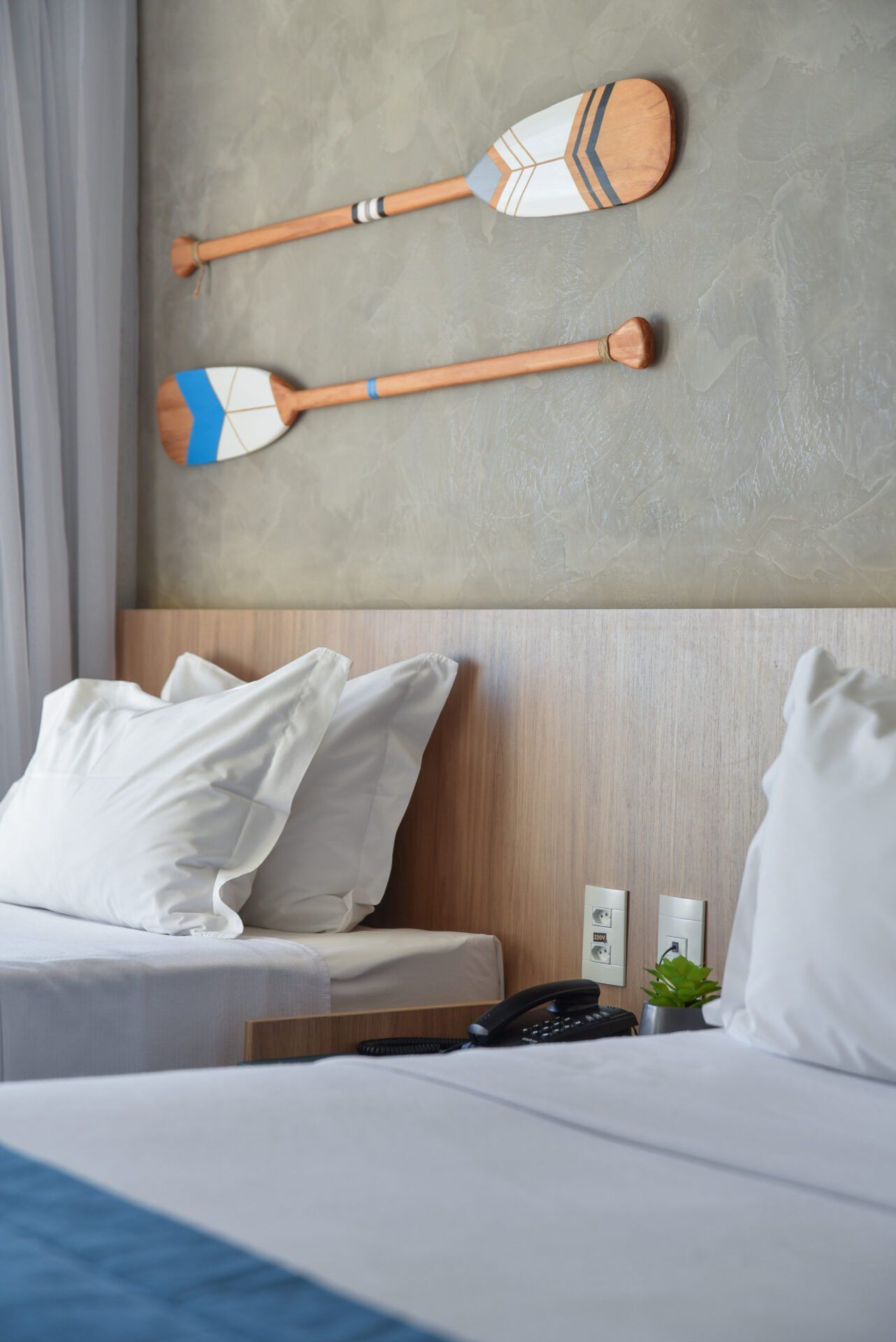 Duas camas com roupa de cama branca, cabeceira de madeira e remos decorativos em uma parede texturizada.