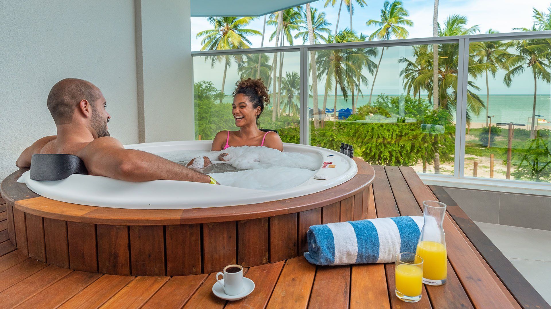 Casal relaxando em uma banheira de hidromassagem ao ar livre com vista para o mar.